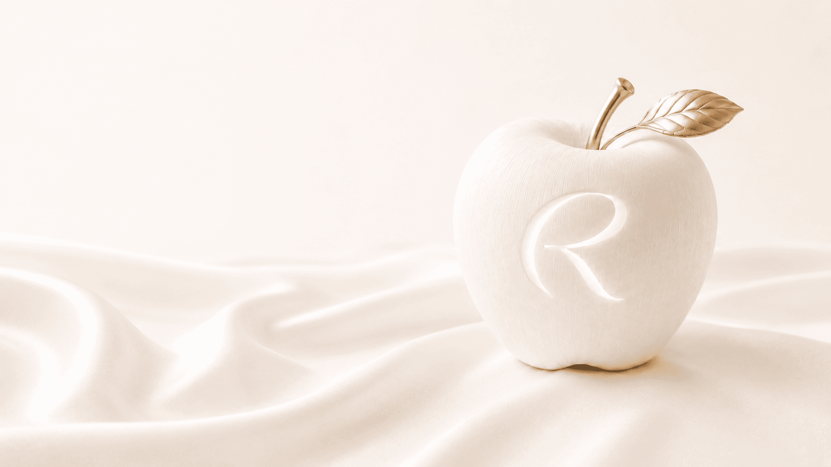 A porcelain apple with a golden R resting on cream silk — the Reflis brand still life